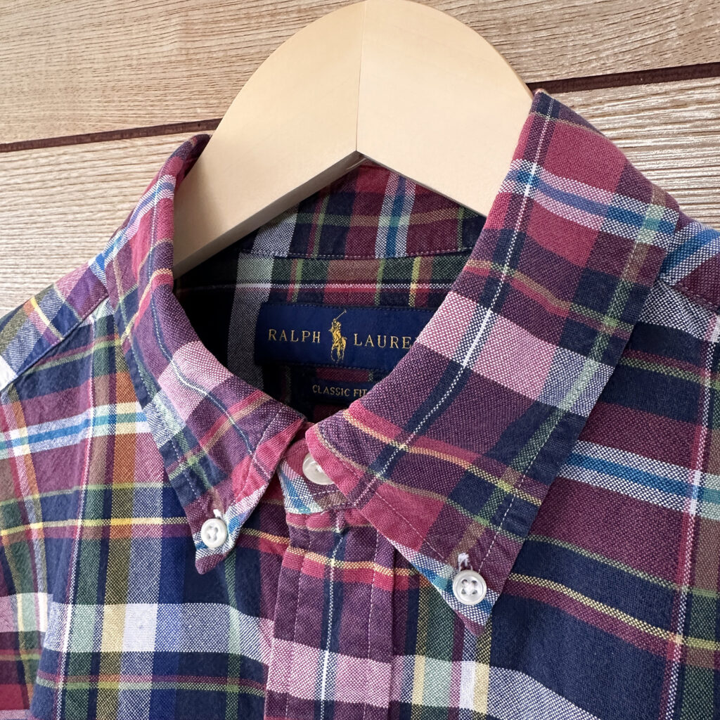 ラルフローレンのマルチカラー・チェックシャツの襟元アップ。木製ハンガーに掛けられ、ボタンダウンの襟先と青いブランドタグがはっきりと写っている。オックスフォード生地特有の、丈夫な質感が伝わる一枚。